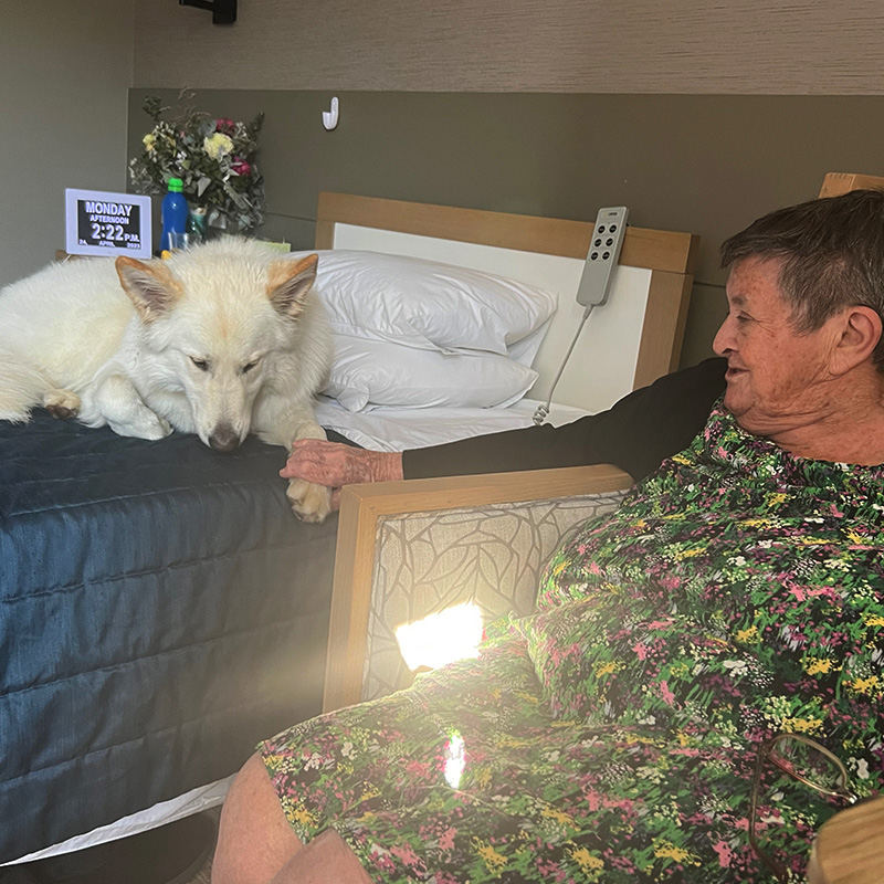 A woman sitting in front of a bed with her dog.